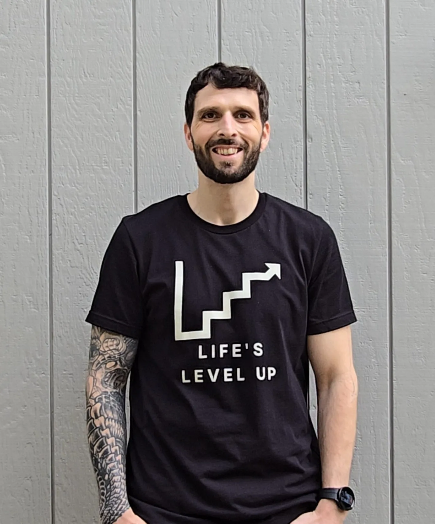 Ken smiling at the camera in a black Life's Level Up tee.